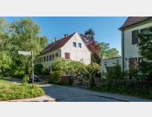 Straßenansicht in einer Wohngegend mit zwei Häusern im traditionellen Stil, roten Ziegeldächern und Fensterläden. Die Umgebung ist von Bäumen und Gärten geprägt, mit einem Straßenschild „Rendtorffstraße“ im Vordergrund.