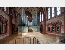 Innenansicht einer historischen Kirche mit roten Backsteinwänden, spitzbogigen Fenstern und einer großen Orgel. Der Holzfußboden und die erhöhte Bühne unterstreichen das zentrale Orgelgehäuse mit zahlreichen Pfeifen und einem Klavierspielpult.