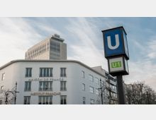 Ein weißes Gebäude mit der Aufschrift „Maison de France“ und „Institut Français“ im Vordergrund. Daneben ein blaues U-Bahn-Schild mit der Liniennummer „U1“ und ein moderner Bürokomplex im Hintergrund.