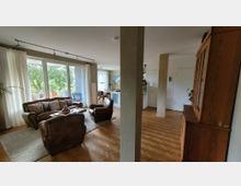 Wohnzimmer mit großem Fenster und Zugang zu einem Balkon, ausgestattet mit braunen Ledersesseln, passendem Sofa, Holztisch und hellen Vorhängen. Im Hintergrund sind ein Essbereich mit Tisch und Stühlen sowie eine Kommode und Pflanzen sichtbar.