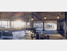 Ein großer, offener Raum im Industrie-Design mit roher Betondecke und freigelegten Balken. Im Vordergrund steht eine Kaffeemaschine auf einer Theke, im Hintergrund sind große Fensterfronten, die Tageslicht hereinlassen, sowie minimalistische Sitzgelegenheiten sichtbar.