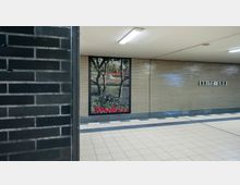 U-Bahnhof mit gefliesten Wänden in neutralen Farben, an einer Wand ein großflächiges Bild eines Parks mit Blumenbeeten. Rechts ist ein Schild mit der Aufschrift „Britz-Süd“ angebracht.