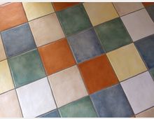 Bunte Keramikfliesen in quadratischer Anordnung, mit abwechselnden Farben in Grün, Blau, Gelb, Orange und Weiß. Die Fliesen haben eine matte Oberfläche und sind symmetrisch verlegt.