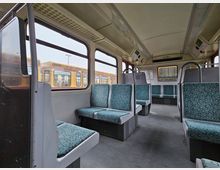 Innenraum einer S-Bahn mit gepolsterten Sitzen in blau-grauem Muster, grauem Boden und großen Fenstern. Durch die Fenster ist eine benachbarte S-Bahn zu sehen, teilweise mit einem Fahrradsymbol gekennzeichnet.