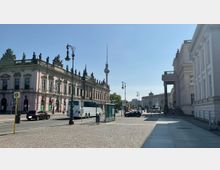 Straßenszene in Berlin mit historischem Gebäude links und modernen Straßenlaternen im Vordergrund. Im Hintergrund ist der Berliner Fernsehturm sichtbar, neben weiteren historischen und modernen Gebäuden.