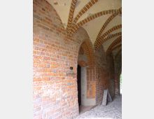 Backsteingewölbter Arkadengang eines historischen Gebäudes mit spitzbogigen Durchgängen, gemauerten Bögen und Kopfsteinpflasterboden.