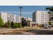 Mehrere Wohnblöcke in Plattenbauweise, umgeben von Grünflächen und einzelnen Bäumen. Im Vordergrund eine Straße, ein geparkter LKW sowie ein einstöckiges Gebäude mit einer Beschriftung "Lucky Inn".