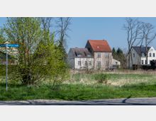 Straßenkreuzung in ländlicher Umgebung mit einem Straßenschild "Göttliner Straße" im Vordergrund, grüner Wiese und Bäumen. Im Hintergrund stehen mehrere Wohnhäuser mit roten und dunklen Dächern.