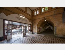 Eingangsbereich eines Bahnhofs mit gelblichen Backsteinwänden und gewölbten Decken. Im Vordergrund sind offene Glastüren, dahinter befinden sich abgestellte Fahrräder und vorbeifahrende Autos; der Tunnel im Hintergrund zeigt Plakate an den Wänden.