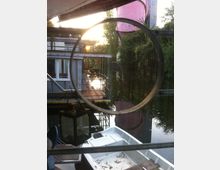 Ansicht eines ruhigen Kanals mit einem kleinen weißen Boot im Vordergrund, umgeben von dichter Vegetation und Gebäudestrukturen. Im Hintergrund sind ein modernes Gebäude mit einer Terrasse und ein großer pinker Wasserturm sichtbar.