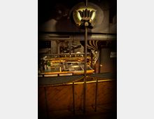 Innenansicht einer stilvollen Bar mit dunkler Holzverkleidung und geschwungenem Tresen. Im Hintergrund eine glänzende, gut ausgestattete Theke mit Spülbecken und Regalen; dekorative, industrielle Elemente und Beleuchtung akzentuieren den Raum.