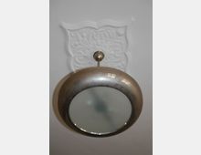 Metallische Deckenleuchte mit rundem, gewölbtem Design vor einer verzierten, weißen Stuckrosette auf einer glatten Decke.