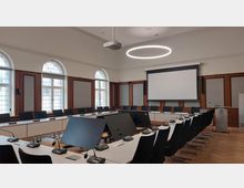 Moderner Konferenzraum mit hufeisenförmiger Anordnung von weißen Tischen und schwarzen Stühlen. Der Raum verfügt über große Fenster mit Rundbögen, Holzwandverkleidung, eine Leinwand an der Stirnseite und eine kreisförmige, leuchtende Deckenlampe.