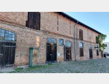 Backstein-Gebäude mit rustikalen Holztüren und Sprossenfenstern, gekennzeichnet als "Pferdestall". Der gepflasterte Vorplatz und einige Begrünungen an den Wänden ergänzen das historische Ambiente.