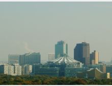 Skyline von Berlin mit modernen Hochhäusern, darunter das charakteristische weiße Zeltdach des Sony Centers. Im Vordergrund ist eine Baumreihe sichtbar, die einen Kontrast zur städtischen Architektur bildet.