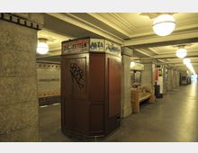 U-Bahn-Station mit gefliesten Wänden und der Aufschrift „Hohenzollernplatz“, einem alten, mit Graffiti versehenden Zigarettenautomaten sowie Sitzbänken und großen, runden Deckenleuchten.