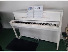 Ein weißes Digitalpiano mit der Marke "Kawai" steht auf einem grünen Teppichboden. Darüber liegt ein aufgeschlagenes Notenbuch, und vor dem Piano befindet sich ein schwarzer Klavierhocker.