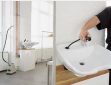 Links: Heller Raum mit modernem Waschbecken auf einem weißen Unterschrank, Kupferrohren, einem Kleiderständer und einem Dampfreiniger. Rechts: Nahaufnahme einer Person, die den Wasserfluss aus einer schwarzen, flexiblen Handbrause über dem Waschbecken reguliert.
