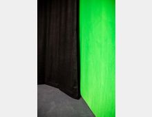 Schwarzer Vorhang links neben einer grünen Wand, die vermutlich als Greenscreen verwendet wird. Der Boden ist dunkel und weist eine glatte Oberfläche auf.