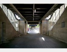 Unterführung am U-Bahnhof Nollendorfplatz mit Sicht auf den Bahnsteigeingang, flankiert von gemauerten Wänden und großen Fensterflächen; darüber eine Stahlkonstruktion mit sichtbaren Trägern. Im Hintergrund ist ein Schild mit der Aufschrift „U-Bhf Nollendorfplatz“ zu erkennen.