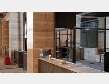 Innenraum eines im Umbau befindlichen Gebäudes mit massiven Stein- oder Marmorsäulen, freiliegenden Metallrahmen und unvollständigen Wand- und Thekenflächen. Auf dem Betonboden stehen Bau- und Reinigungsgegenstände, während im Hintergrund weitere offene Räume und Trennwände sichtbar sind.