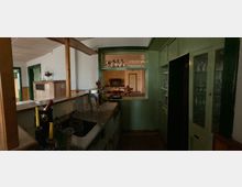 Dunkler Innenraum einer Bar oder Küchenzeile mit einer Theke, einem Spülbecken und Gläsern. Im Hintergrund ist durch ein offenes Fenster ein weiterer Raum mit Holztischen und einem Klavier sichtbar.