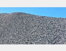 Ein großer Haufen grauer Schottersteine vor einem klaren blauen Himmel. Die Steinoberfläche wirkt uneben und erstreckt sich hügelig in die Höhe.