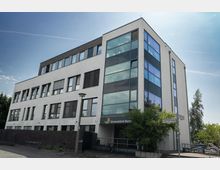 Modernes mehrstöckiges Gebäude mit weißer Fassade und großen Glasflächen, genutzt als Schmerzklinik in Berlin. Vor dem Eingang befindet sich ein Baum sowie ein Straßenschild mit der Beschriftung "Günter-Littin-Straße".