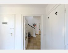 Heller Hausflur mit weißen Wänden, einer Tür mit Glaseinsatz in der Mitte, die in einen Flur mit Treppenaufgang führt. Rechts befinden sich Einbauschränke mit kleinen Ausschnitten, links eine Innentür mit Sichtfenster.