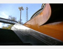 Treppe neben einer orange gefliesten Gebäudewand, die zu einem Schild mit den Hinweisen „Internationales Congress Centrum“ und „ZOB“ führt; im Hintergrund der Funkturm und ein Straßenlampenmast vor einem blauen Himmel.