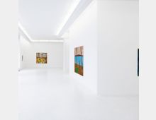 Weiße, minimalistische Galerie mit glatten Wänden und glänzendem Boden, beleuchtet durch lineare Deckenleuchten. An den Wänden hängen farbenfrohe, geometrisch-abstrakte und landschaftliche Gemälde.