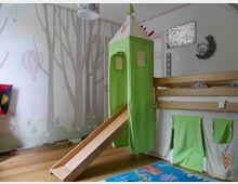 Kinderzimmer mit Hochbett aus hellem Holz, das mit grünen Stoffvorhängen zu einem Spielbereich gestaltet ist. An das Bett ist eine Holzrutsche angebaut, und die Wand ist mit einem Wald- und Heißluftballonmotiv dekoriert.