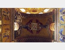 Decke eines historischen Kirchenraums mit aufwendigen Mosaiken, goldener Verzierung und gemalten Engeln. Rundbögen mit natürlichen Lichtquellen rahmen die Szene.