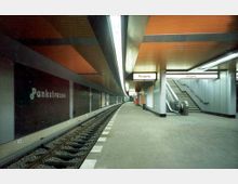 U-Bahn-Station mit dem Namen "Pankstraße". Die Station hat einen Bahnsteig mit gleisnahen Sitzgelegenheiten, orangefarbene Deckenpaneele, beleuchtete Ausgänge, eine Rolltreppe und ein Treppenhaus auf der rechten Seite.