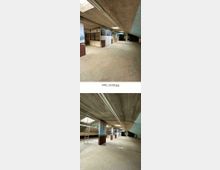 Ein leerer, betonierter Innenraum mit niedriger Decke und sichtbaren Rohrleitungen, umgeben von Trennwänden mit Landschaftsmotiven. Tageslicht fällt durch mehrere Oberlichter ein, und eine Leiter lehnt an einer Wand.