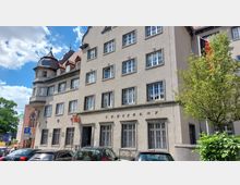 Mehrstöckiges historisches Bankgebäude mit beige-farbener Fassade, großen rechteckigen Fenstern und der Aufschrift „Kreisbank“. Links ist ein Rundturm mit Ziegeldach, vorne parken Autos, und rechts steht ein Baum.