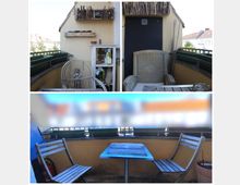 Small apartment balcony with a yellow stucco wall and black railing, lined with rectangular planter boxes. The space includes a wicker chair, a small table with two wooden chairs, and a white storage shelf beneath a sloped roof overhang.