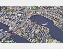 Luftaufnahme eines städtischen Gebiets in Berlin mit markierten Gehwegen und Verbindungen. Der Bahnhof Ostkreuz und Treptower Park sind mit grünen S-Bahn-Symbolen hervorgehoben, während ein „Loft Office“ am Wasser sowie Bushaltestellen markiert sind. Ein See und Wohngebäude dominieren die Umgebung.