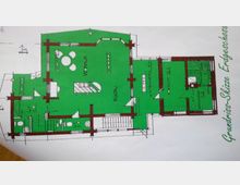 Grundrissskizze eines Erdgeschosses mit grün markierten Bereichen, die verschiedene Räume wie "Wohnen", "Küche", "Vorräume", sowie einen "Saunabereich" umfassen; zentrale Elemente sind Treppen, Türen und Sanitäranlagen, die detailliert eingezeichnet sind. Die Außenwände sind durch dickere Linien und die Raumgrößen in Quadratmetern angegeben.