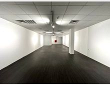 Leerer Innenraum mit weißen Wänden, dunklem Bodenbelag und einer Rasterdecke mit eingebauten Leuchten und Belüftungsgittern. Am Ende des Raums ist ein roter Feuerlöscher an der Wand angebracht.