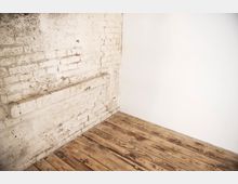Ecke eines Raumes mit einer weißen Backsteinwand, einer glatten weißen Wand und einem Boden aus Holzplanken mit sichtbarer Maserung.
