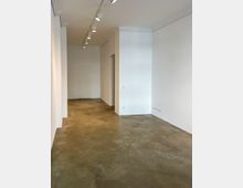 Leerer Innenraum mit weißen Wänden, poliertem Betonboden und einer Reihe von Deckenspots an der Decke. Im Hintergrund ist eine Tür ohne sichtbare Verzierungen zu erkennen.