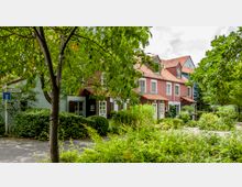 Blick auf eine Reihenhaus-Siedlung mit roten Fassaden und weißen Fenstern, umgeben von dichtem Grün und Bäumen. Im Vordergrund steht ein Straßenverkehrsschild, das eine Sackgasse anzeigt.