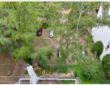 Ansicht von oben auf einen Innenhof mit Bäumen, parkenden Autos und gepflasterten Wegen. Im Vordergrund ist ein Balkon mit einer geschlossenen Sonnenschirmhülle, im Hintergrund eine teilweise von Efeu bedeckte Hauswand.