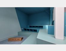 Raum mit blauen Wänden und Stufen, die integrierte quadratische Ablagefächer enthalten. Die Decke ist dunkelblau mit weißen Punkten, und in einer Ecke liegt ein brauner Karton.