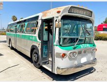 Ein silber-grüner, vintage Linienbus mit der Aufschrift „6 Sepulveda Blvd“ auf der Frontanzeige steht auf einem sonnigen Parkplatz. Der Bus zeigt deutliche Gebrauchsspuren, und die Einstiegstür ist geöffnet.