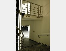 Treppenhaus mit modernen Metallgeländern, das zu einem Raum mit Marmorboden und der Beschriftung „Planetariumssaal“ führt. Wände und Beleuchtungselemente sind schlicht gestaltet.