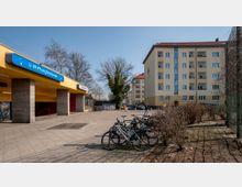 Außenansicht des U-Bahnhofs Jungfernheide in Berlin mit gelber Fassade und blauer Beschilderung, daneben ein Fahrradständer mit mehreren Fahrrädern. Im Hintergrund sind Wohnhäuser und kahle Bäume zu sehen, die Umgebung wirkt städtisch.