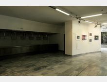 Geräumiger Empfangsbereich mit hellen Marmorböden, einer Garderobe mit nummerierten Kleiderhaken an der linken Seite und einer beleuchteten Wand rechts, an der mehrere gerahmte Bilder hängen.